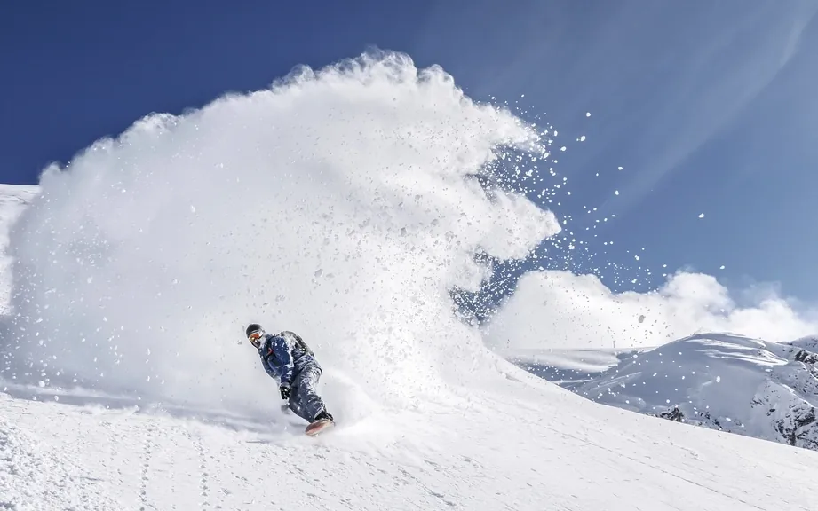 Snowboarder throwing a spray of powder on a bluebird day